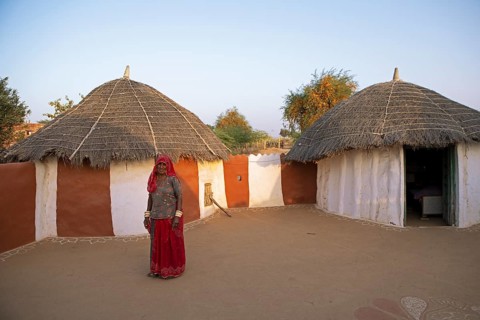 Indian woman, 55 years old, desert dweller, behind typical round buildings in the Thar Desert or