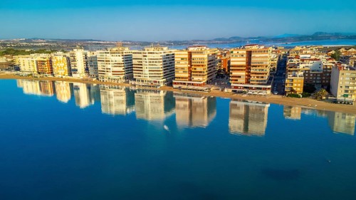 Aerial view of torrevieja skyline reflecting on calm mediterranean sea at sunrise, with colorful
