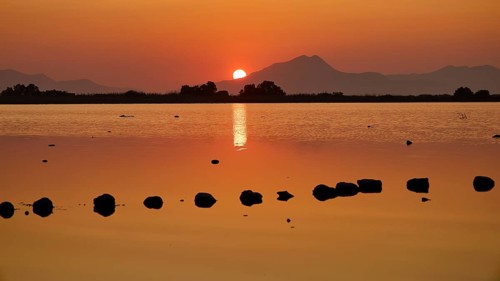 Warm sunset light reflected in the calm lake with mountain backdrop, salt lake, Tigaki, nature
