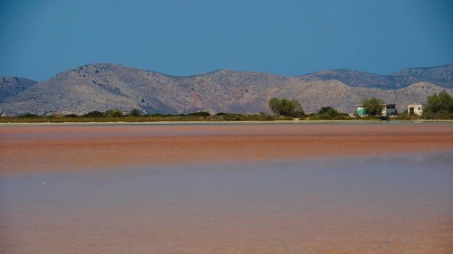 Mountainous landscape with calm lake and small huts under a bright blue sky, salt lake, Tigaki,