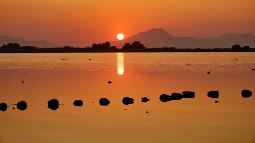 Glistening sunset with warm tones and mountain silhouette, salt lake, Tigaki, nature reserve, hydro