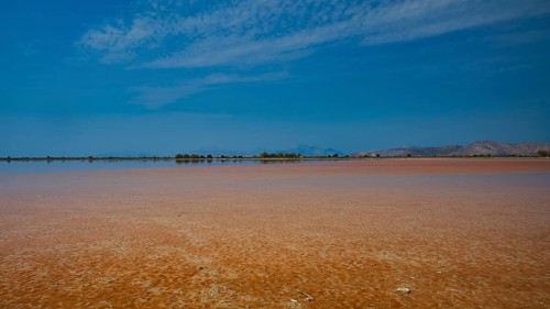 Wide, open landscape with a lake under a narrow blue sky, quiet atmosphere, salt lake, Tigaki,