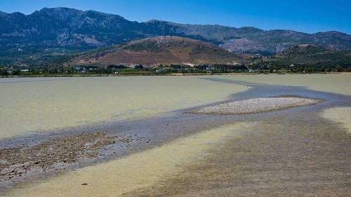 A lake with a long gravel bank and mountains in the background under a blue sky, salt lake, Tigaki,