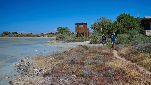 Two hikers on a path next to an observation tower and vegetation, salt lake, Tigaki, nature