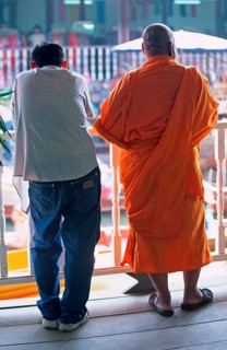 A monk and another man watch the hustle and bustle at Damnoen Saduak Floating Market, Thailand,