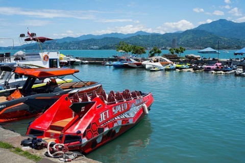 A red jet boat in the foreground of a harbor surrounded by other boats and mountains in the