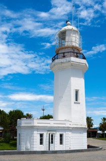 White lighthouse against a blue sky with some clouds and palm trees in the background, lighthouse,