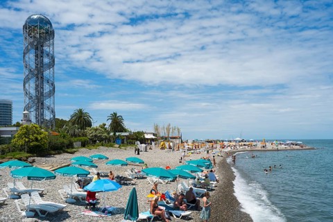 Beach with many visitors under umbrellas, a view of the sea and a distinctive tower in the