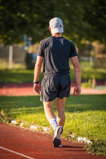 A person in sportswear runs on a running track in the middle of a green, summer environment,