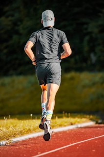 Person running on red covering in grey sports dress in daylight, triathlon, Calw, Germany