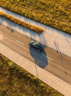 Aerial view of moving car and long shadows on paved road, BMW i7 electric car, deer e-car sharing,