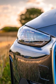 Close-up of a car headlight in the evening, reflecting the surroundings of a field, BMW i7 electric