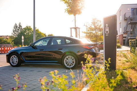 Black BMW at a charging station in an urban environment at sunset, BMW i7 electric car, Deer