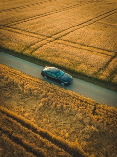 A dark car drives on a paved road surrounded by cornfields at dawn or dusk, BMW i7 electric car,