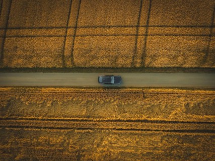 Top view of a car driving on a narrow path between golden fields in quiet countryside, BMW i7