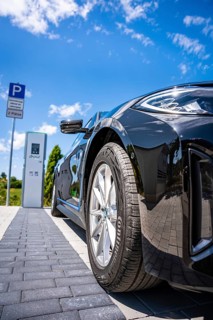 Close-up of a black car next to a parking machine under a blue sky, BMW i7 electric car, Deer