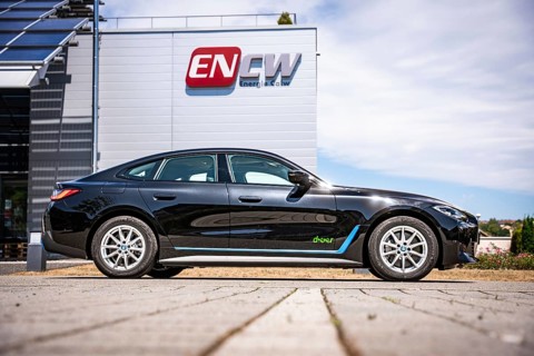 Black car in front of a building with a large company logo under blue sky, BMW i7 electric car,
