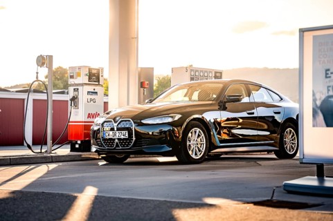 Black car at a gas station in the evening sun with modern architecture, BMW i7 electric car, Deer