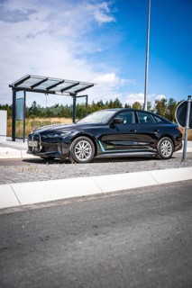 Black car at a modern bus stop under blue sky, BMW i7 electric car, Deer e-Carsharing, Calw,