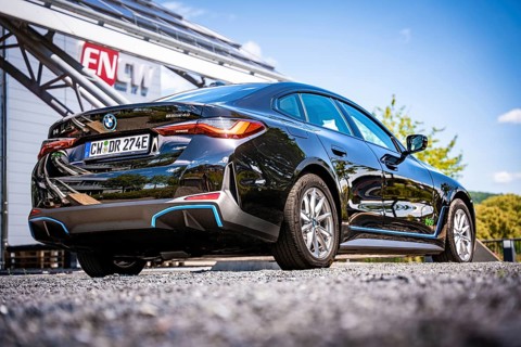 Rear view of a black car in front of a modern building with ENCW logo and blue sky, BMW i7 electric