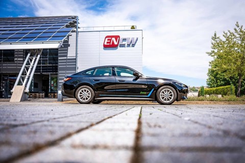 Black car on the side of a modern building with ENCW logo on a paved path, BMW i7 electric car,