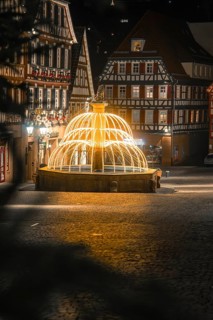 Nocturnal scene with illuminated fountain surrounded by traditional half-timbered houses, Calw,