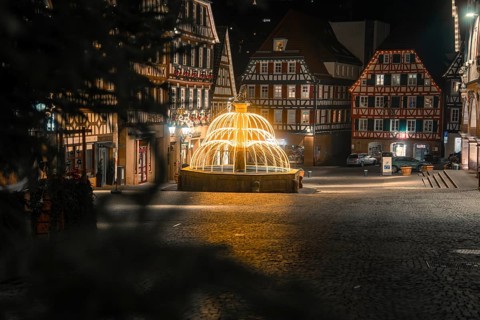 Idyllic night scene with illuminated fountain and traditional buildings in the city center, Calw,