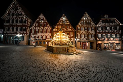 Illuminated fountain in a historic city center with half-timbered buildings at night, Calw, Black