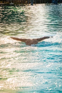 A swimmer in the pool with arms spread out, the water surface shimmers in the light, triathlon,