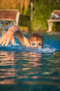 A man actively swims in the pool in sunshine and creates water splashes, Triathlon, Calw, Germany