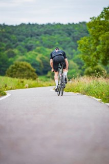 A cyclist rides on a winding road through a wooded area, Triathlon, Calw, Germany