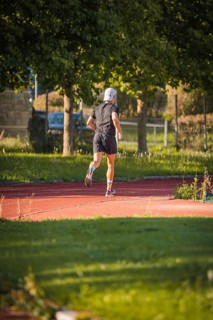A jogger runs on a red track in the countryside, surrounded by trees on a sunny day, triathlon,