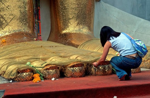 A young woman places flowers on the toes of the standing Buddha at Wat Indrawihan, Bangkok,