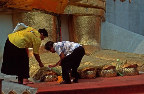Women place flowers on standing Buddha's toes at Wat Indrawihan, Bangkok, Thailand, December 2002,