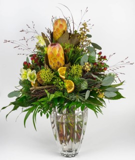 Exotic flower arrangement with protea, Christmas rose and berries in a glass vase, presented