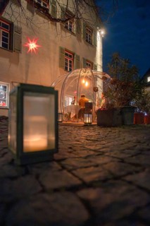 An illuminated dome at night on a stone path flanked by a large candle with windows in the
