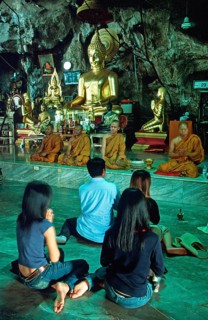Buddha statue, monks and believers praying, Wat Tam Sua monastery near Krabi, Thailand, December