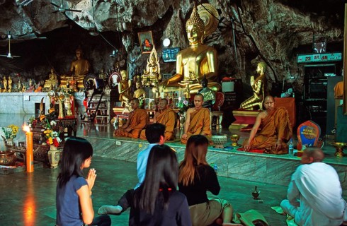 Buddha statue, monks and believers praying, Wat Tam Sua monastery near Krabi, Thailand, December