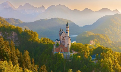 Neuschwanstein Castle in the midst of a fairytale alpine panorama during sunrise surrounded by