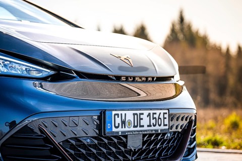 Detailed view of the front end of a stylish black car in front of a forest, electric car Cupra,