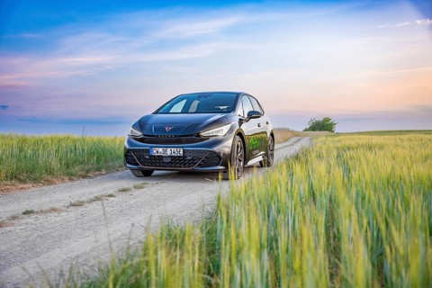 A Cupra drives along a rural path surrounded by fields and an impressive sunset in the background,