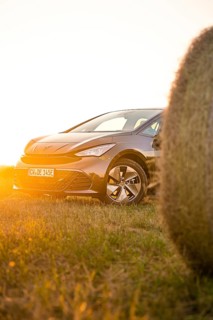 Car in the golden light of sunset in a meadow next to a hay bale, electric car Cupra, e-car