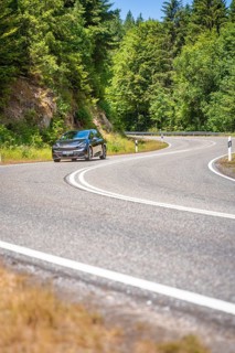 Black car on winding country road along green forests in sunny ambiance, Cupra electric car, e-car