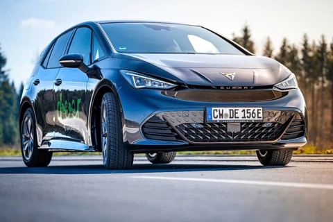 Black car on a road with forest in the background under clear sky, electric car Cupra, e-car