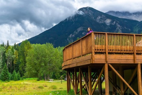 Tourist standing on a wooden deck, admiring the breathtaking view of mount robson, the highest peak