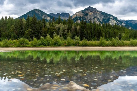Calm waters reflecting the lush forest and majestic mount robson under a cloudy sky create a serene