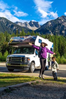 Happy mother and son are jumping in front of their recreational vehicle near mount robson in the