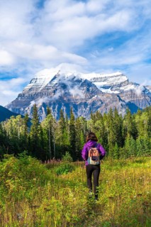 Female hiker walking through a meadow toward the majestic mount robson, the highest peak in the