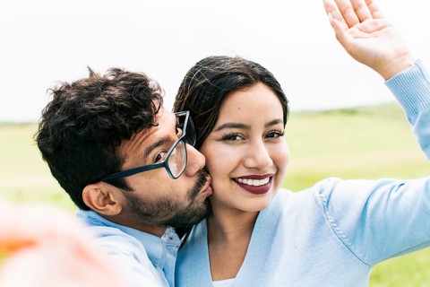 Selfie of young happy couple kissing in the field. Cute couple in love taking a selfie in the