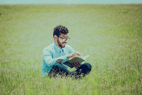 Young man on the grass reading a book, A person sitting on the grass reading a book, concept of